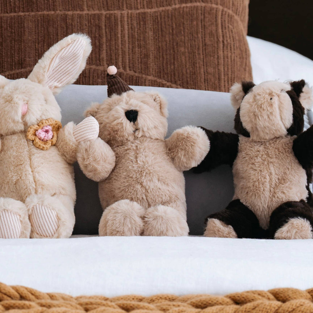 Three plush toys, including a rabbit, bear, and zebra, sitting on a white surface with a brown textured background.