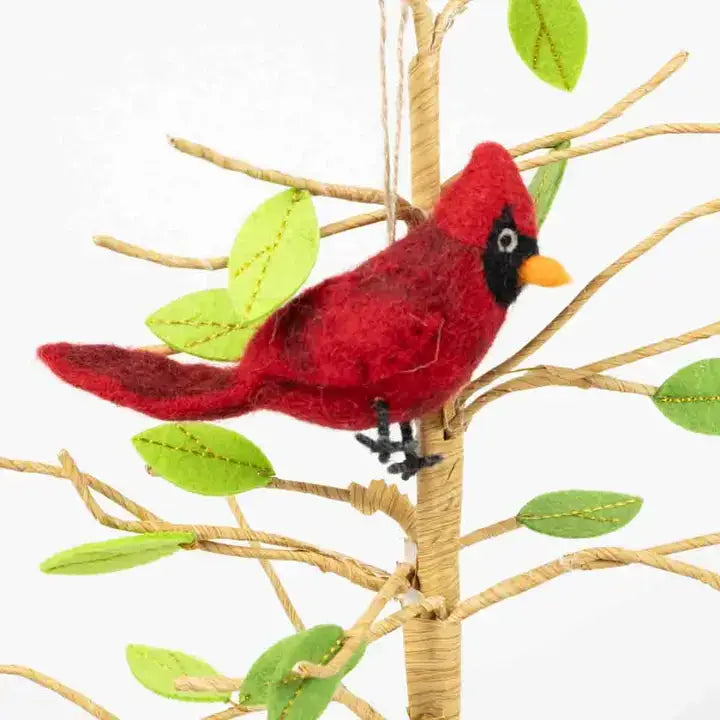 Red cardinal bird ornament on a branch with green leaves against a white background