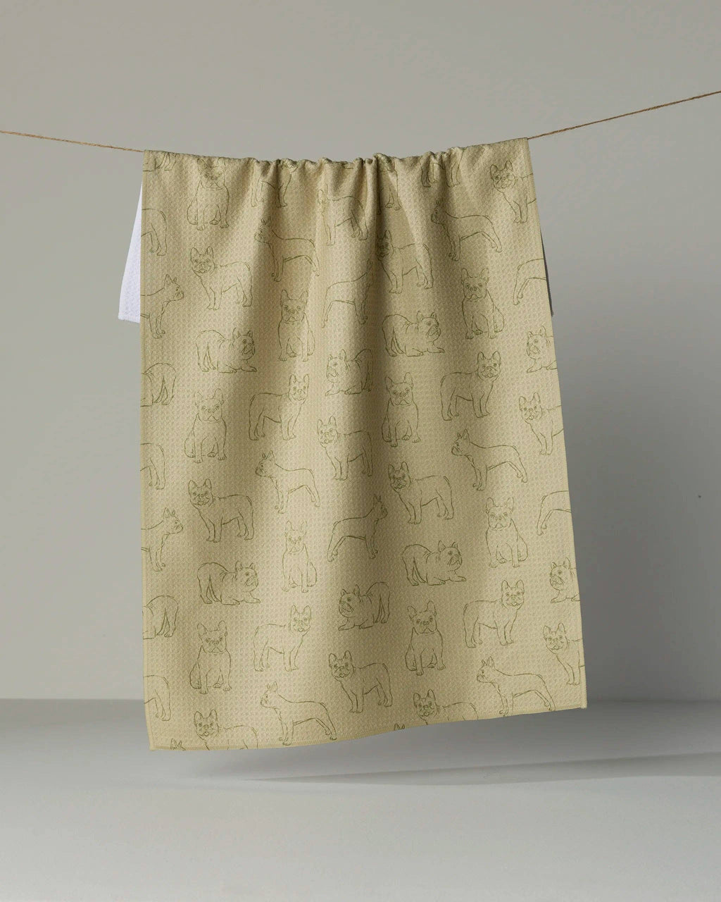 A gathered fabric panel or curtain in a warm beige color, printed with a repeating pattern of simple line drawings of dogs, hanging from a thin string against a plain gray studio background.