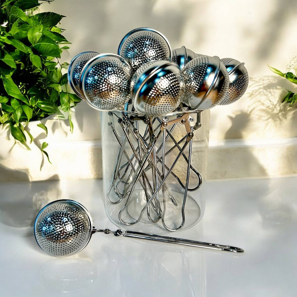 Set of metal tea infusers with a clear stand on a light surface.