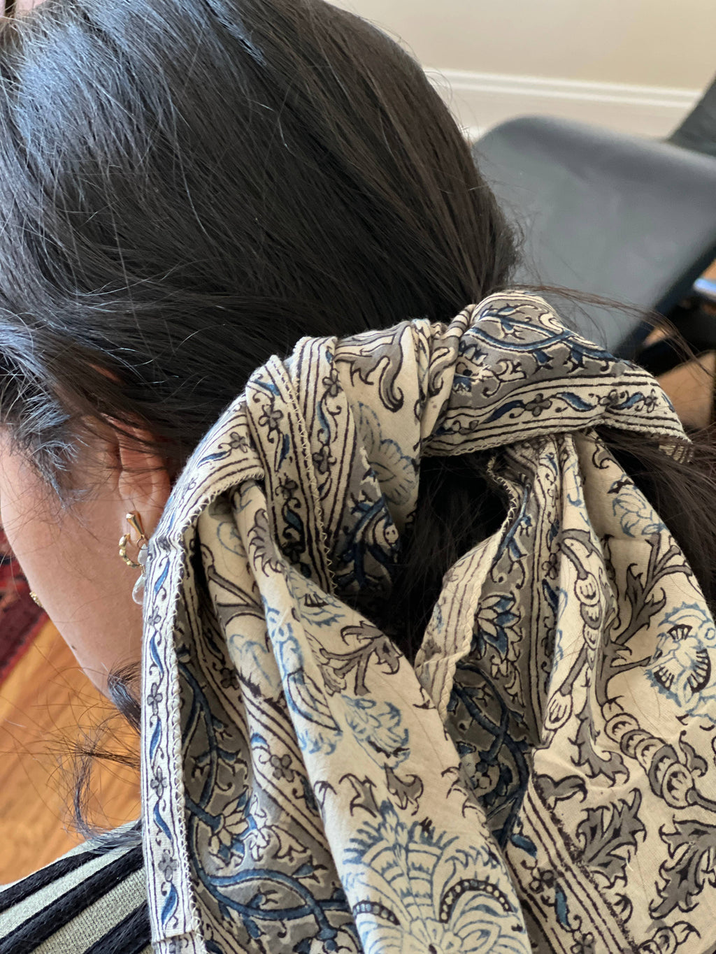 A close-up shot of a person from the back wearing a cream-colored scarf with a blue and gray floral paisley pattern tied around the head.