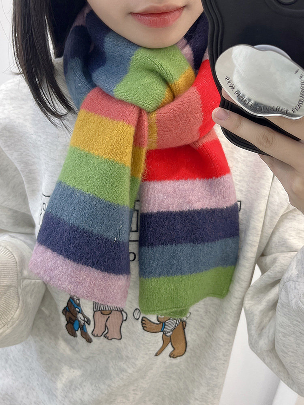 A close-up of a person wearing a fuzzy, multicolored striped scarf. The scarf features horizontal stripes of navy blue, pink, light pink, green, yellow, orange, and red.