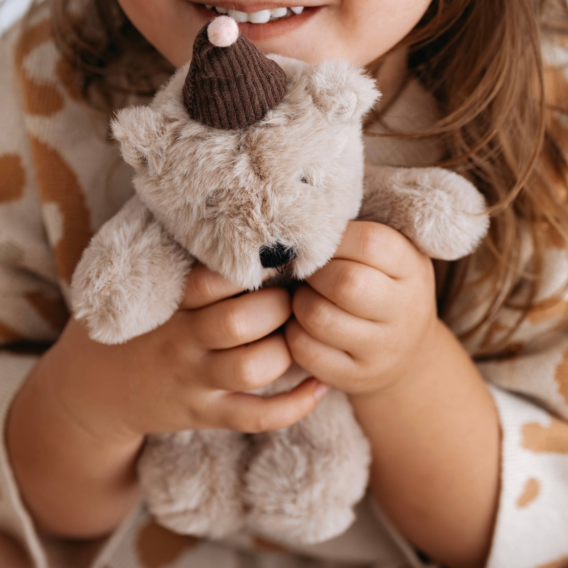 Child holding a small teddy bear with a brown hat