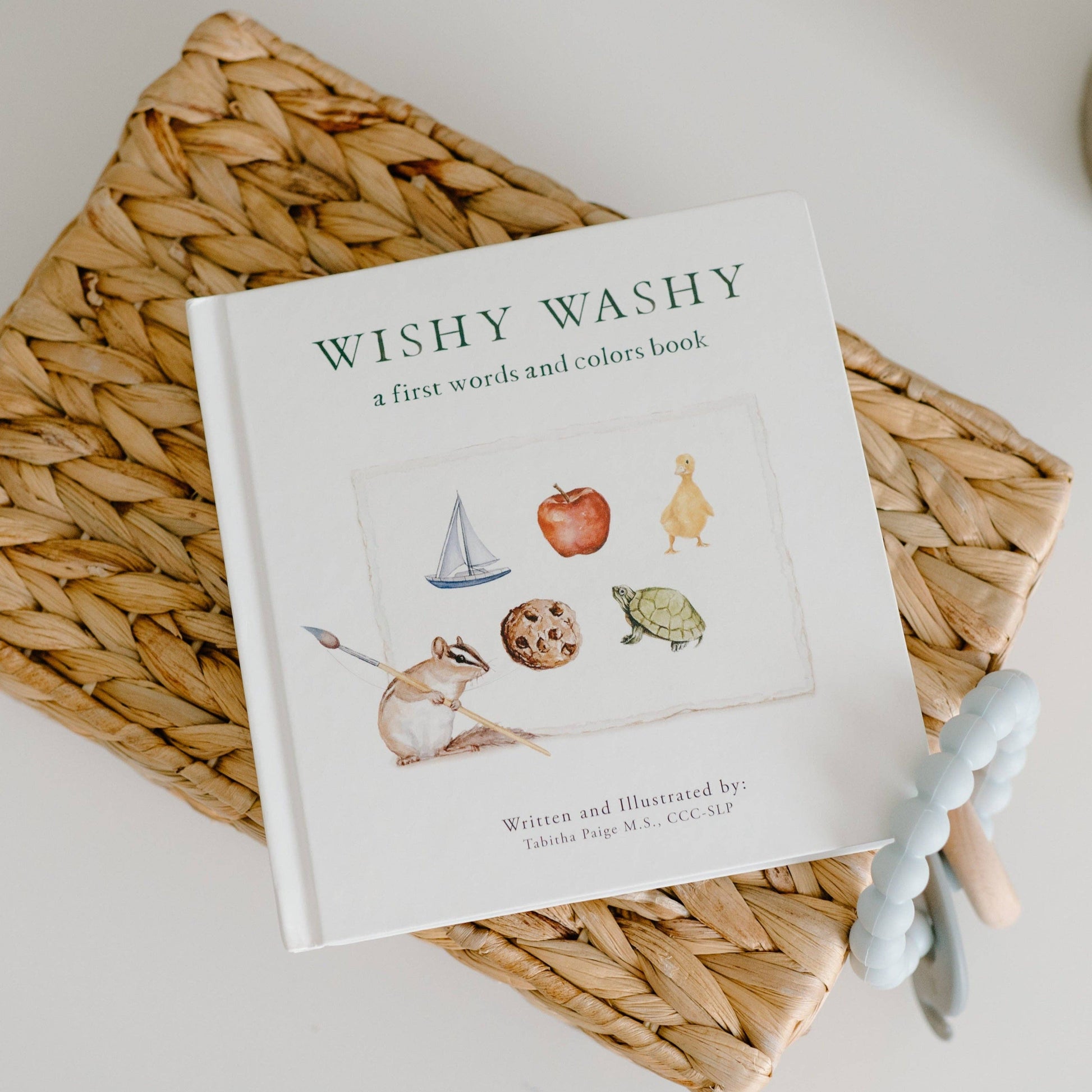 Children's book titled 'Wishy Washy' on a woven mat with a teething toy.