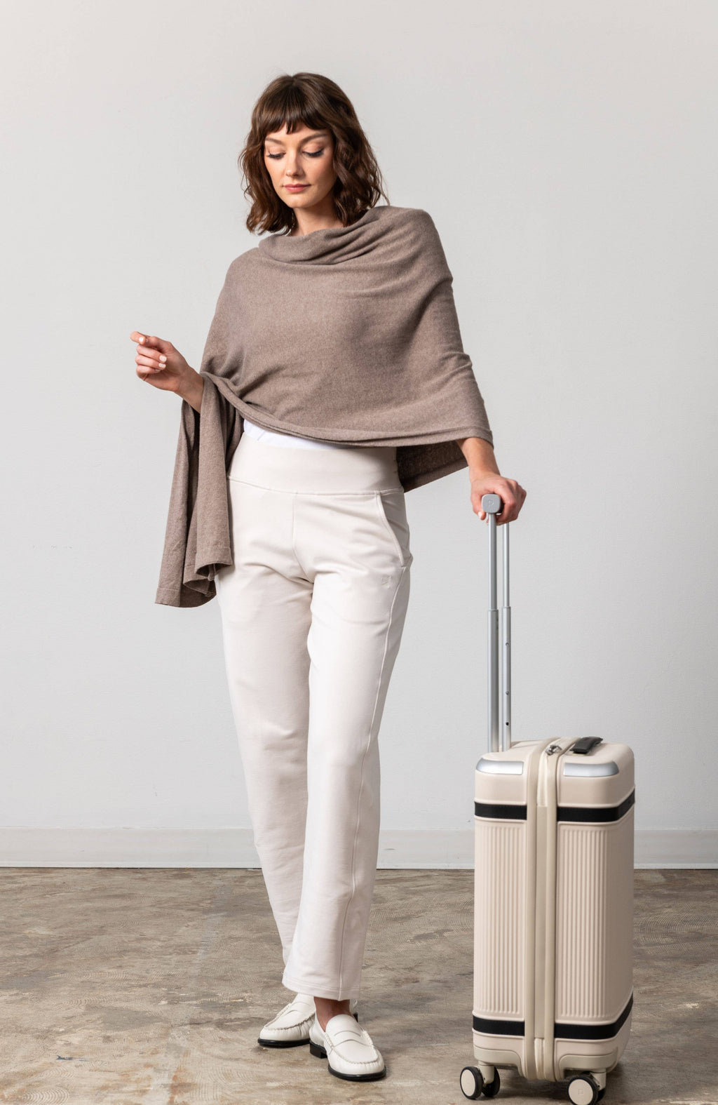 Woman holding a beige suitcase against a plain background