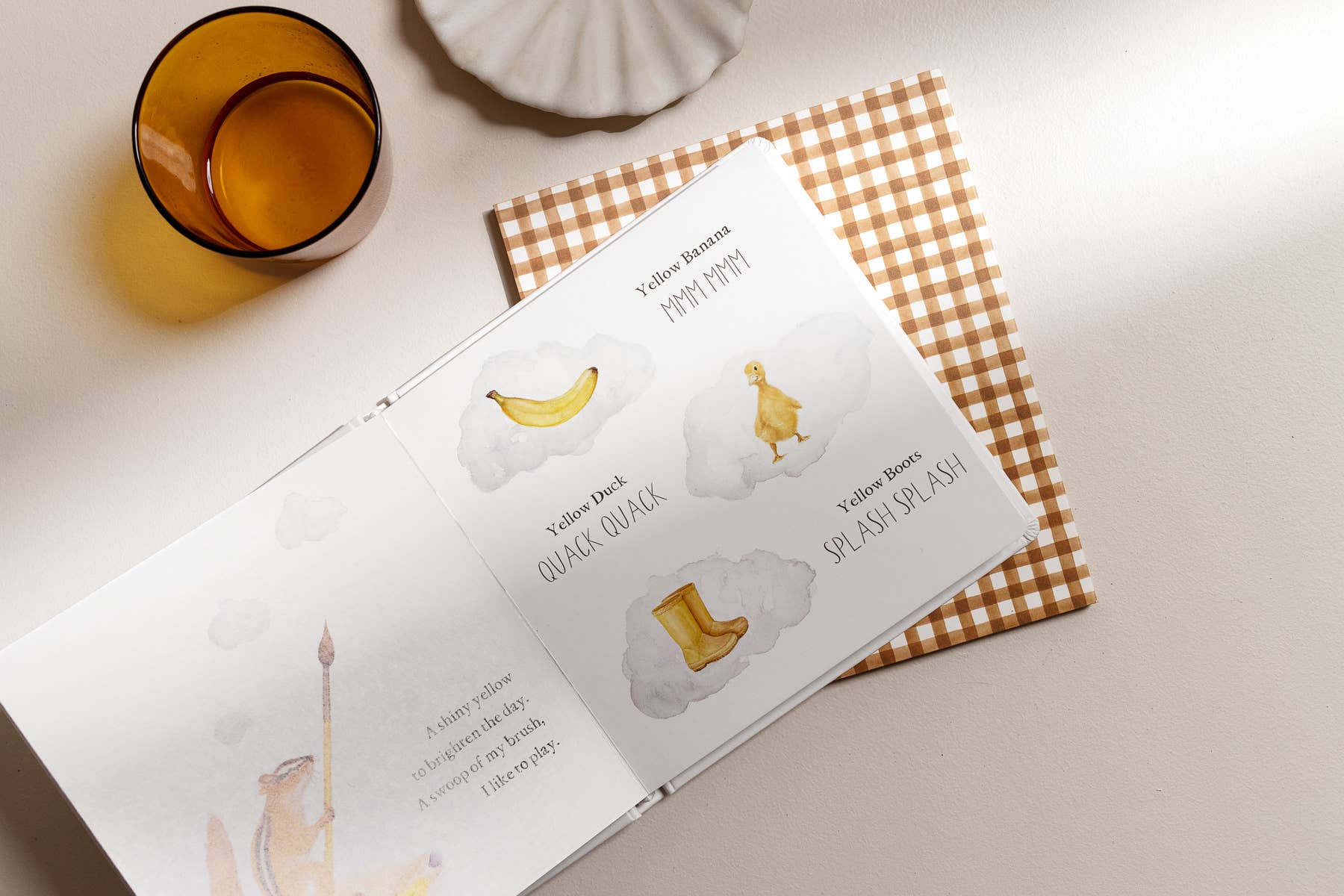 Open book with illustrations of a banana, cloud, and boot on a checkered fabric background.