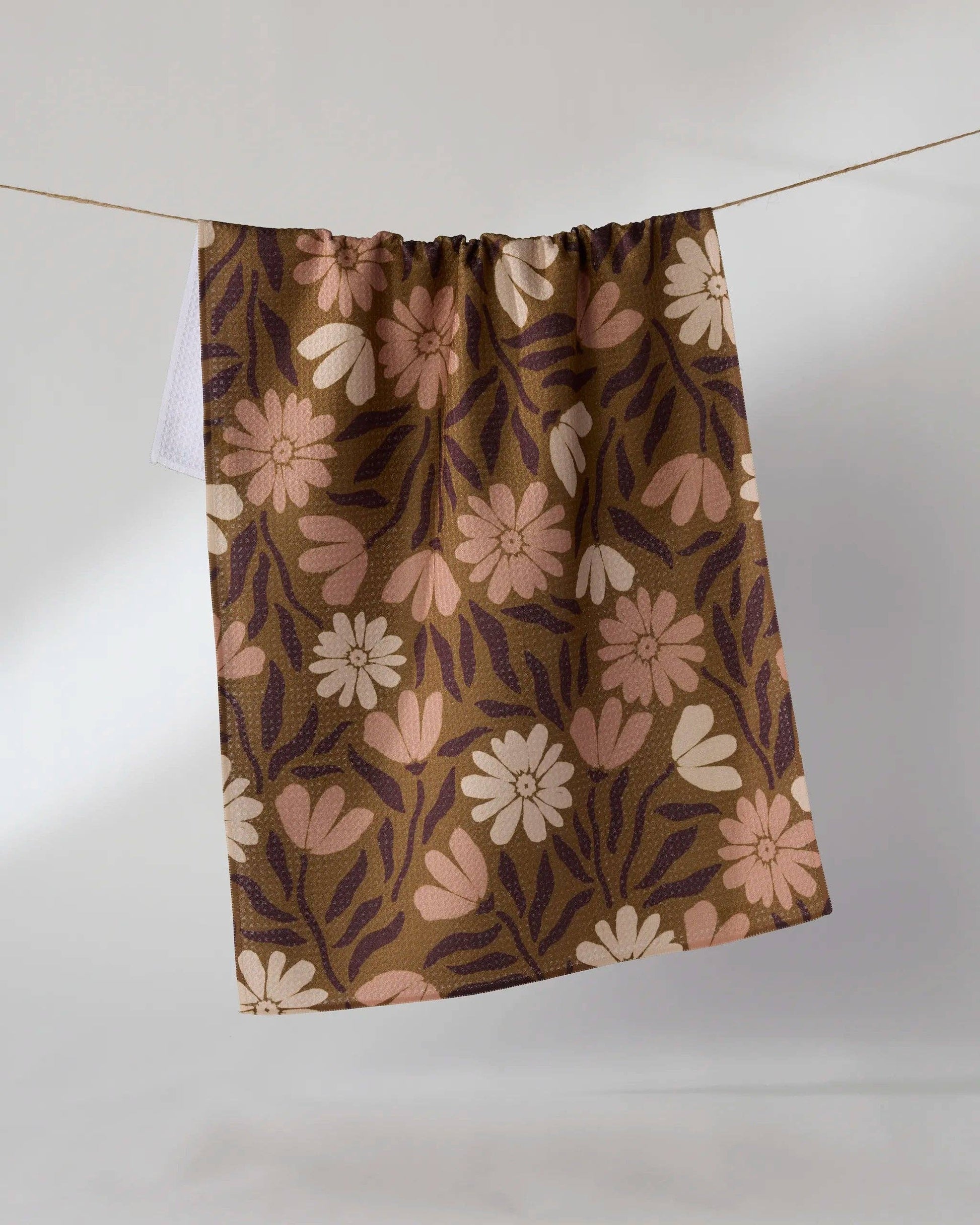 A curtain panel with a retro floral pattern in brown, beige, and pink, hanging from a thin wire against a plain light gray background.