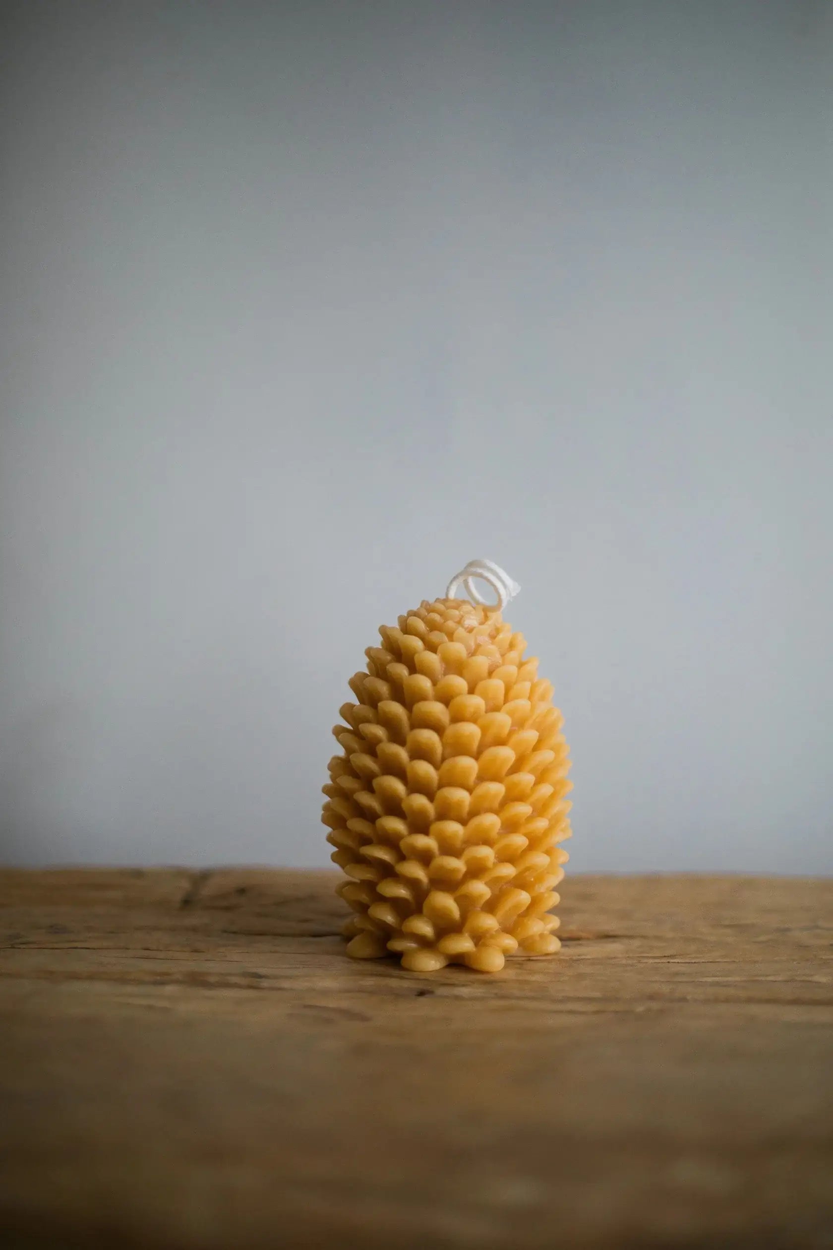 Beeswax candle shaped like a pine cone on a wooden surface with a gray background