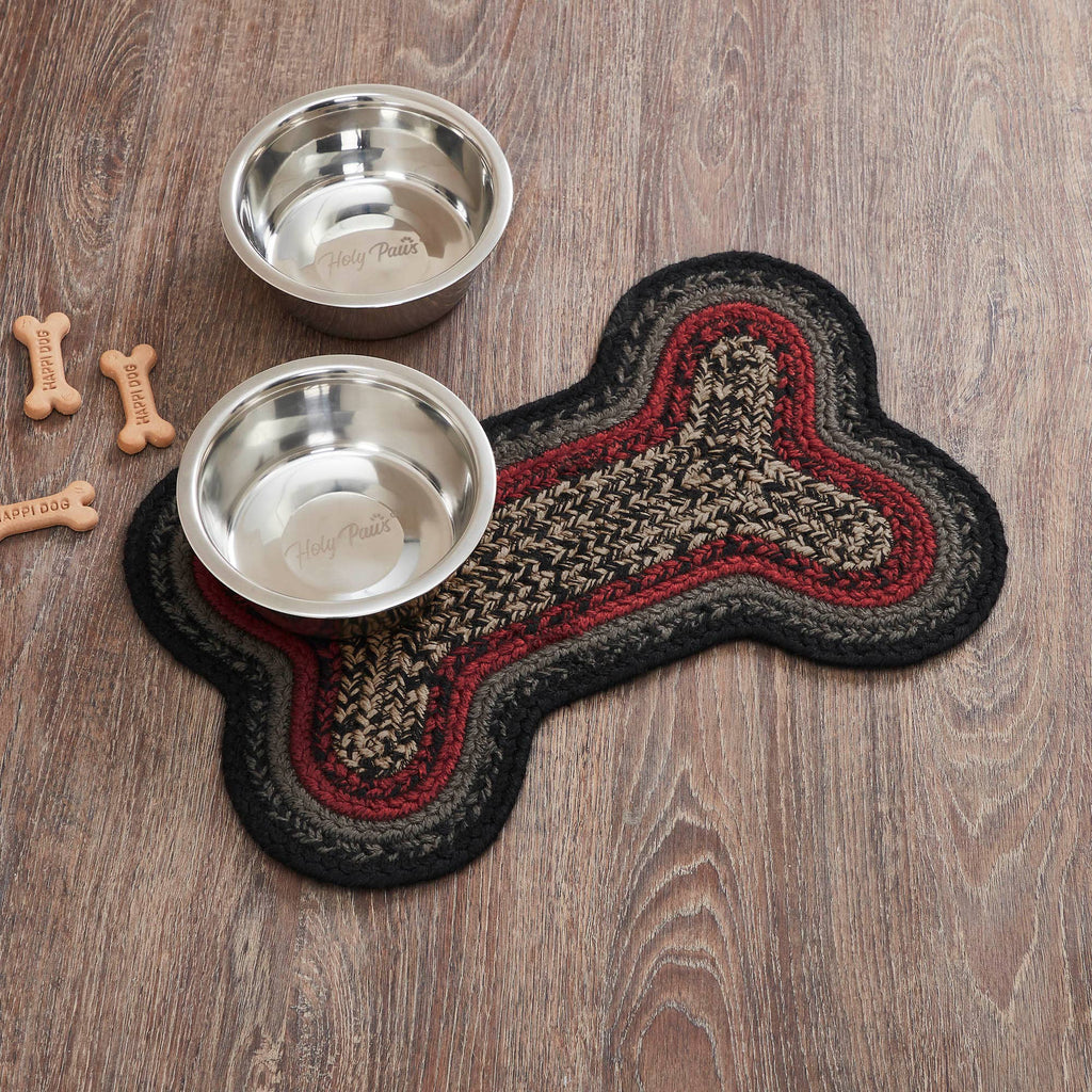Two metal dog bowls on a bone-shaped braided mat with dog bones on a wooden surface.