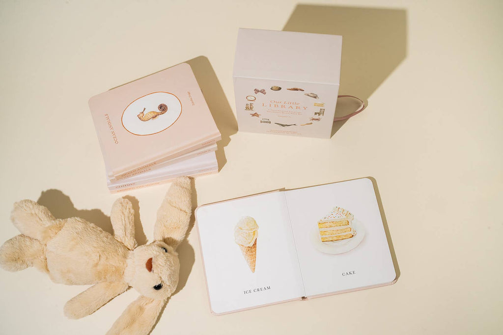 Children's books with illustrations of a teddy bear, ice cream cone, and cake on a beige surface.